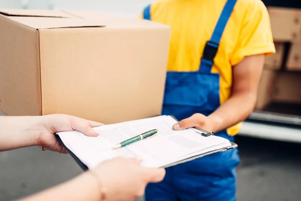 Customer signing a moving form while a mover holds a packed box